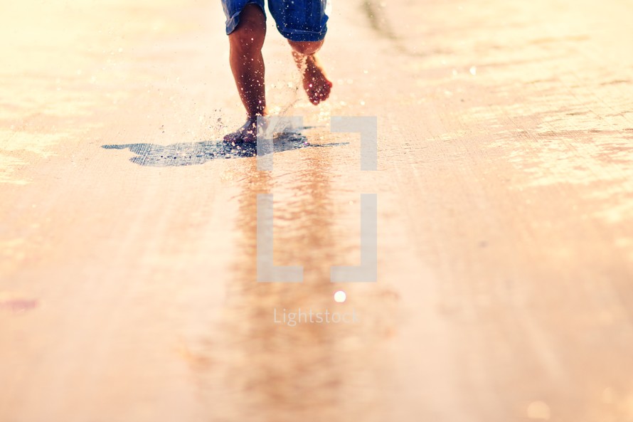 A young boy runs through water and makes a splash