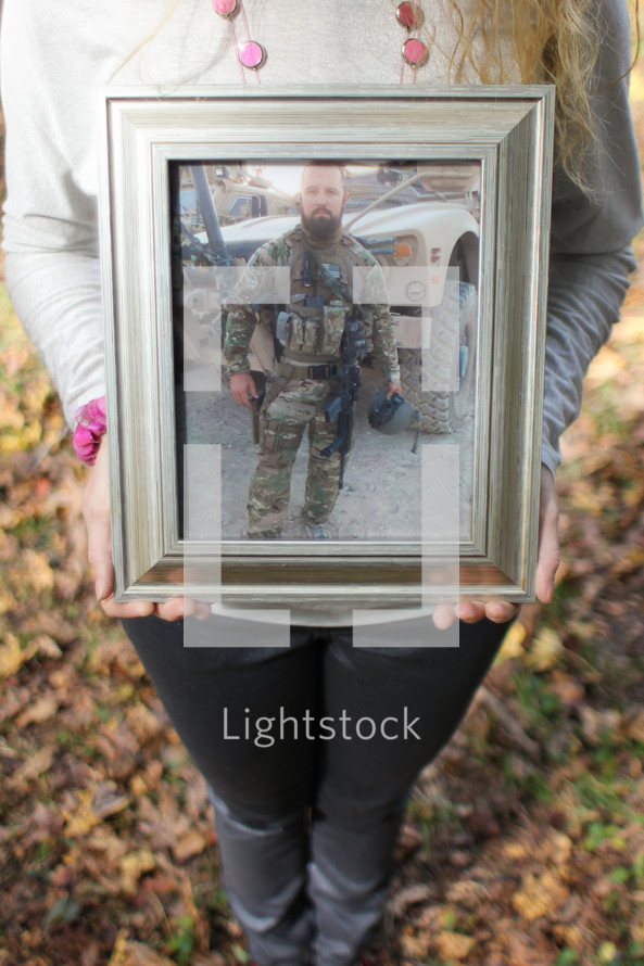 A woman holding a framed photo of a soldier.