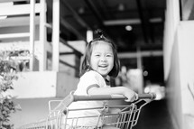 a toddler girl sitting in a shopping cart 