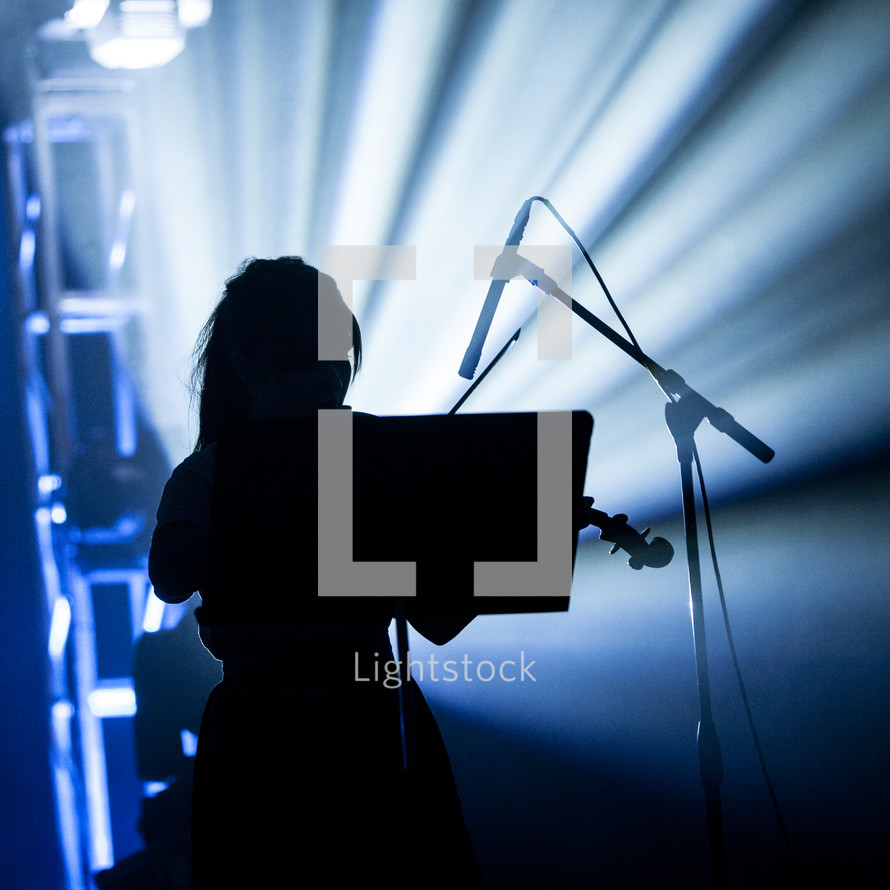 A silhouetted woman playing the violin on stage
