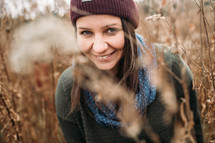 a smiling woman standing in a field of tall brown grasses