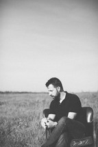 a man sitting outdoors in a leather chair in a field praying 