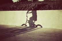 The shadow of a young boy riding his bicycle on the sidewalk
