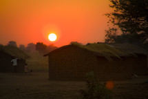 sunset over a thatched roof hut