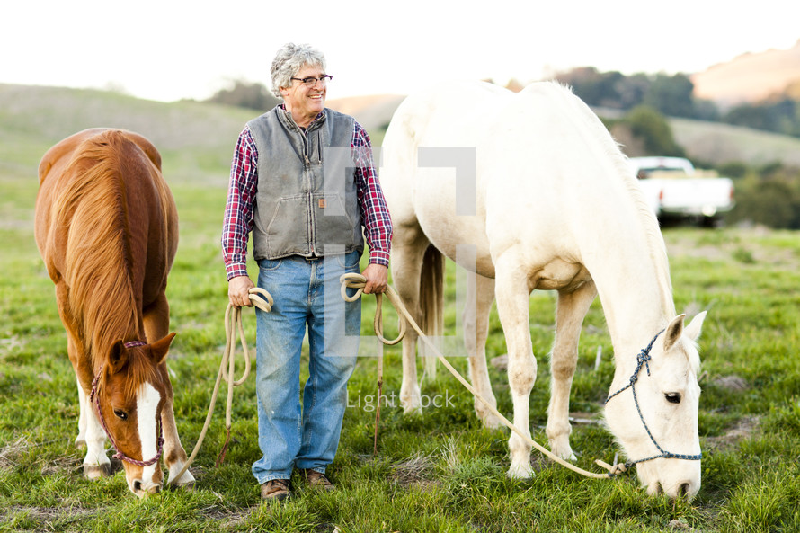 man leading horses to graze farm country hillside