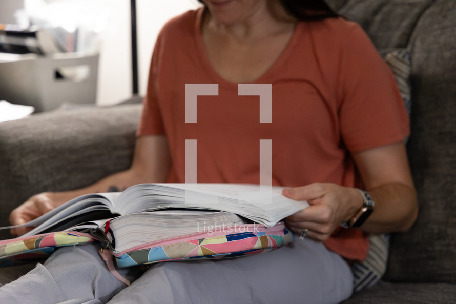 Woman in orange shirt sitting on sofa holding Bible and study book in her lap during Bible study time in her discipleship group