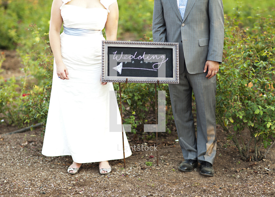bride and groom standing in front of a sign with the words WEDDING