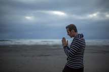 man with praying hands standing on a beach 