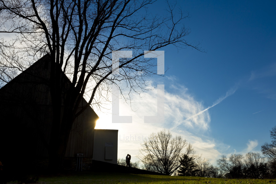 silhouette of a couple kissing by a barn 