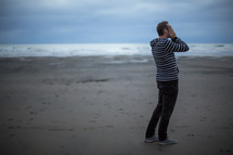 man standing on a beach covering his face 