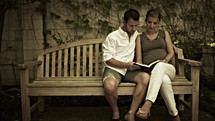 A man and woman reading the Bible on a bench.