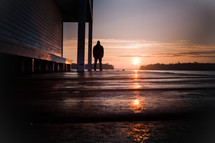 A man looks towards a sunrise on a dock. 