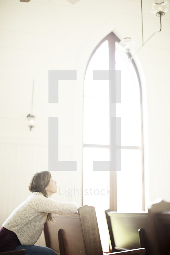 a woman looking up to God sitting in a church pew 