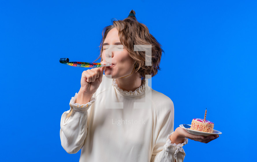 Happy birthday woman making wish - candle on cake. Girl smiling, celebrating anniversary. Young stylish lady on blue background. High quality photo