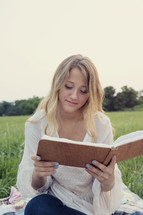 woman sitting in the grass reading a journal.