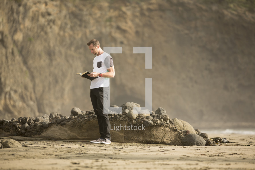 man standing on a beach reading a Bible 
