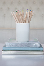 colored pencils in a ceramic cup on a stack of books 