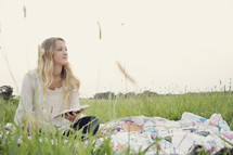 woman reading a book outdoors on a blanket in the grass 