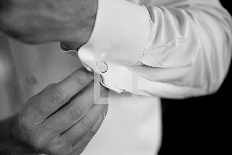 A man attaching a cuff link on a dress shirt.