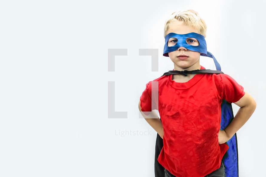 Little  boy dressed as superhero with red shirt and blue mask and cape on white background. 