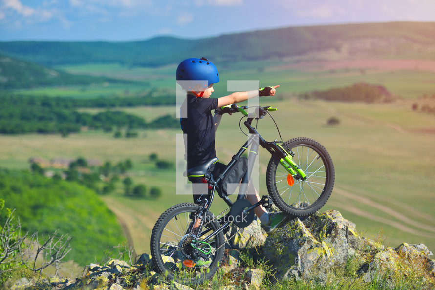 child stands next to his mountain bike on mountains edge and looks at the beautiful scenery