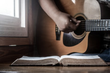 a person playing a guitar next to an open Bible 