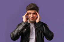 Young man having headache, blood pressure, studio portrait. Guy putting hands on head, isolated on violet background. Concept of problems, medicine, illness. High quality