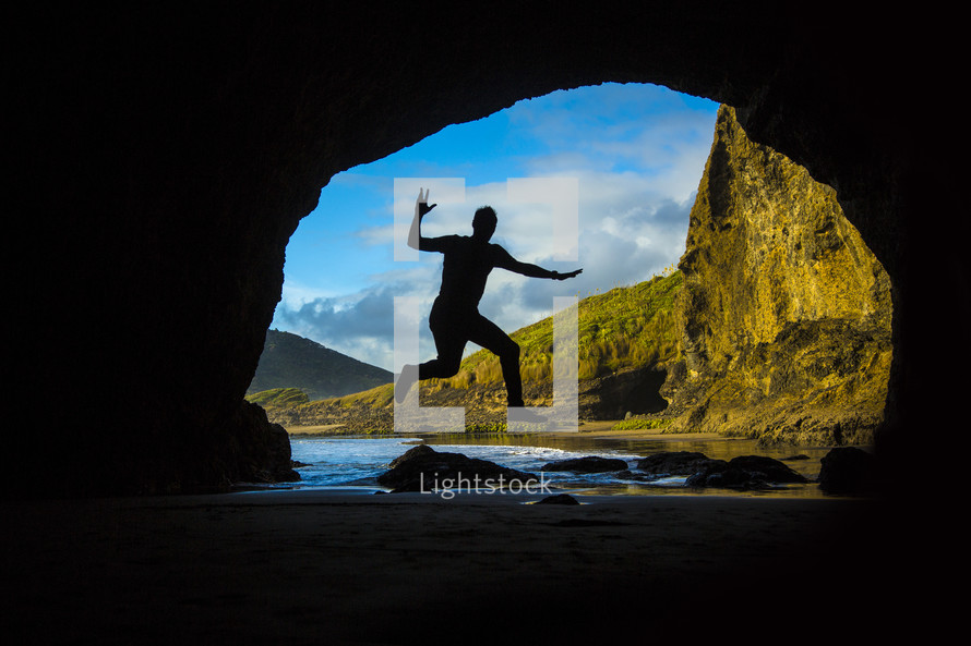 silhouette of a man leaping in the entrance of a cave 
