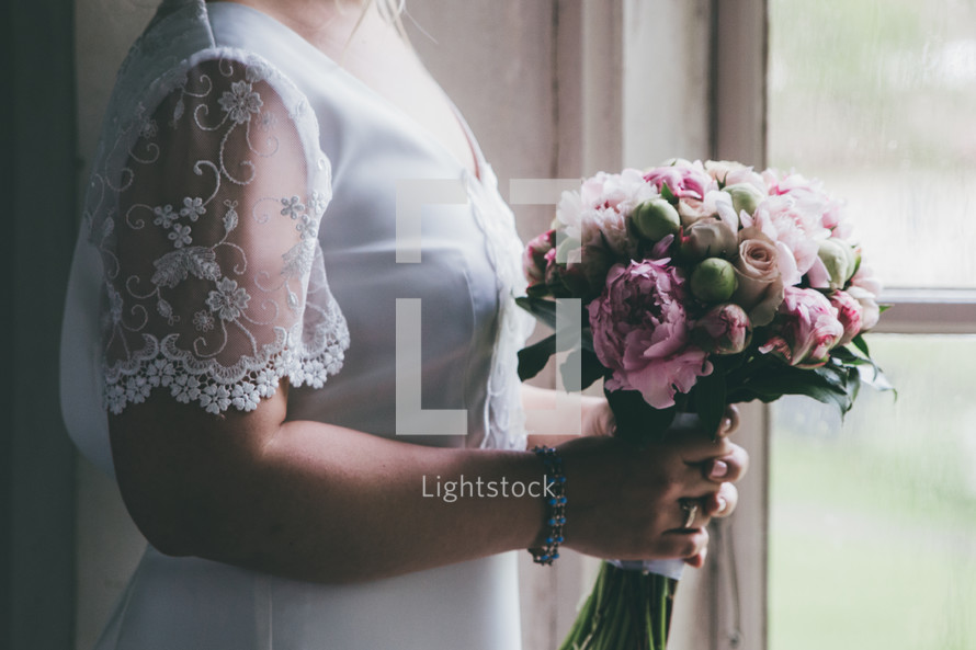 a bride holding a bouquet standing in a window 