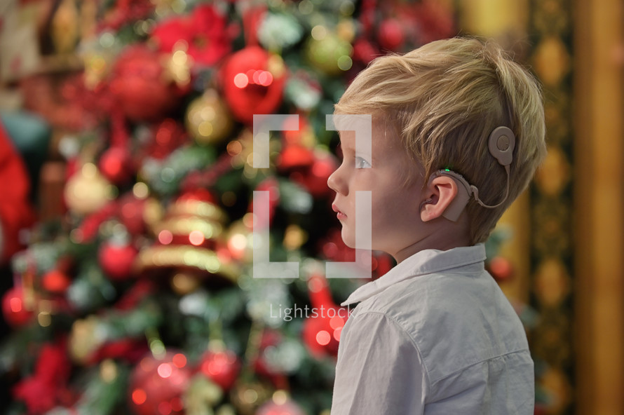A Boy with Cochlear Implants standing in front of a Christmas tree 