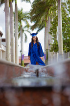 a graduate in cap and gown standing under palm trees 