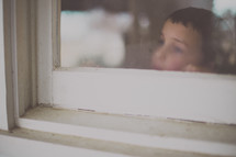 A young boy looks out of a window.