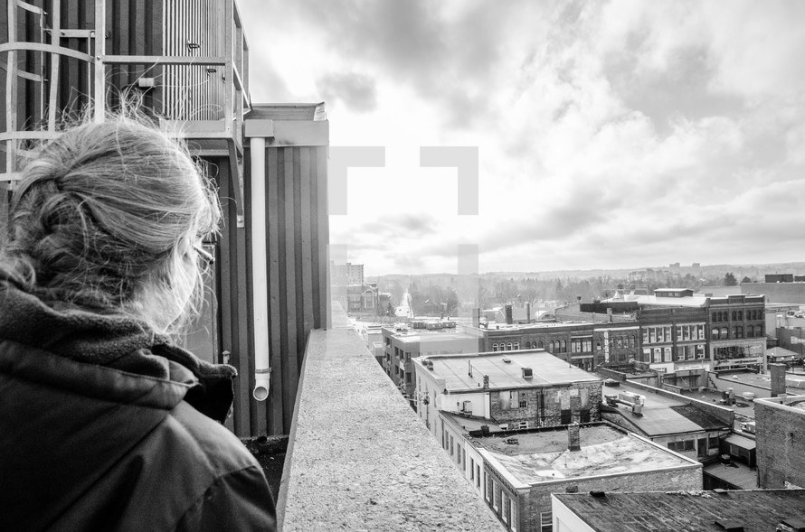 woman on a balcony looking at rooftops in a city 