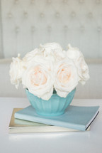 A blue vase of white roses on a stack of books.