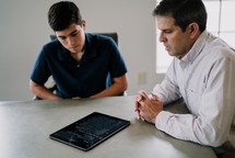 father and son reading Bible verses off of a tablet 