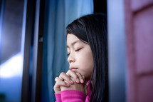 a girl child praying in an open window during quarantine 