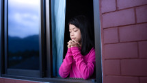 a girl praying in an open widow during quarantine 