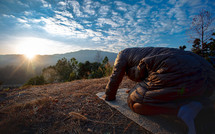 a man kneeling in prayer on a rug outdoors 