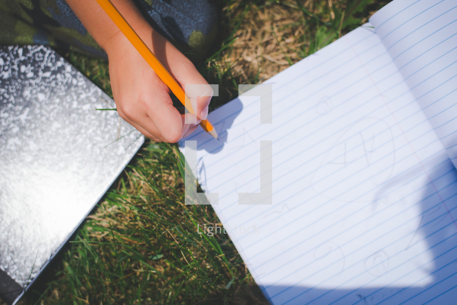 boy writing in a notebook in the grass