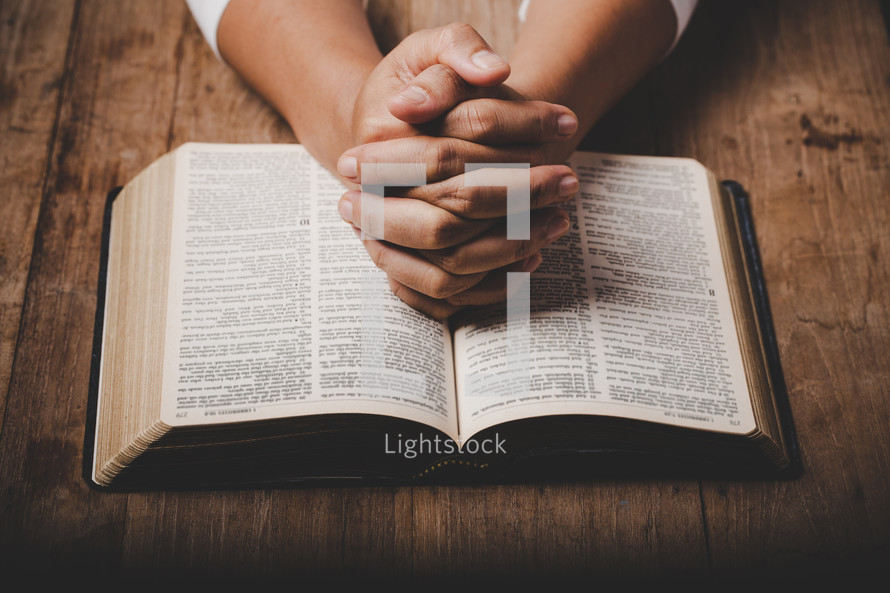 Woman praying with hands on her Bible