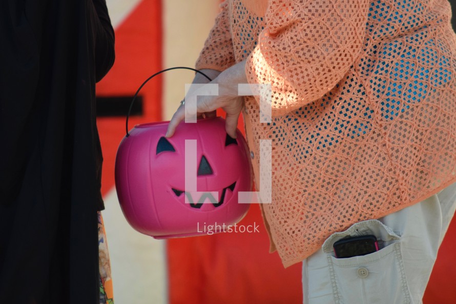 a woman holding a jack-o-lantern Halloween bucket passing out candy 