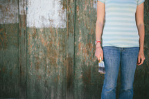 Teen holding paintbrushes near a half painted wood fence.