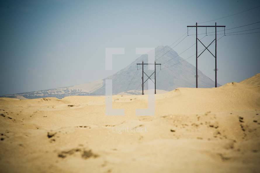Power poles in a desert with a mountain in the background