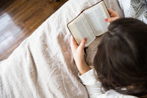 young woman reading a Bible in her bed