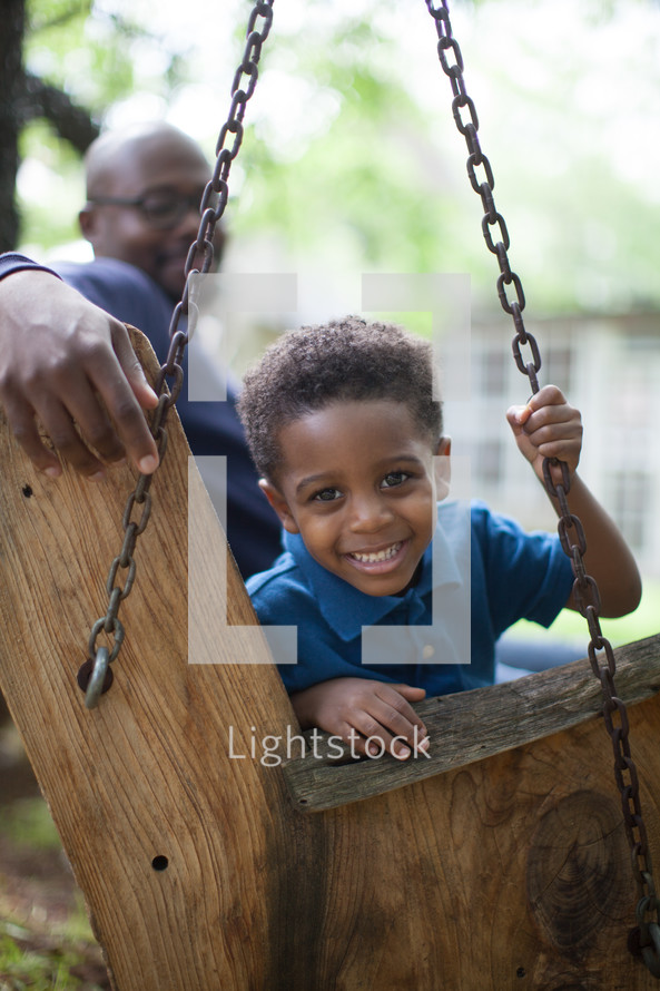 A father and son sitting on a wooden swing.