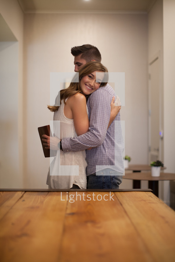A young man and woman embracing near a wooden table.