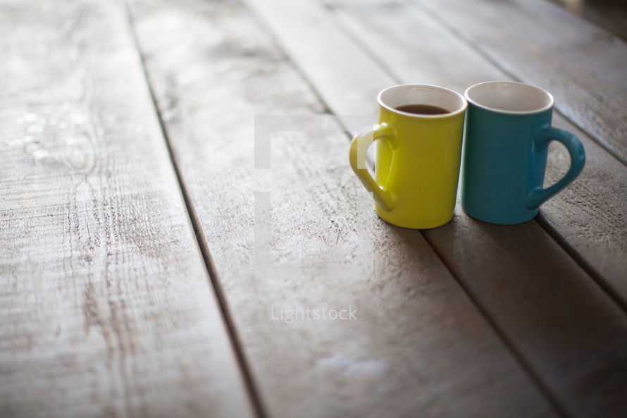 Yellow and blue cups of coffee on a wooden table.