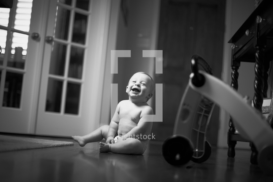 A smiling little boy sits on the floor.