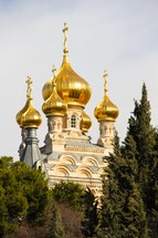 Ornate Orthodox Church with gold turrets surrounded by trees.