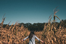 a woman walking through a corn field 